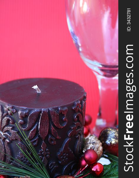 Dark candle with a christmas wreath and a wine glass on a red background. Dark candle with a christmas wreath and a wine glass on a red background
