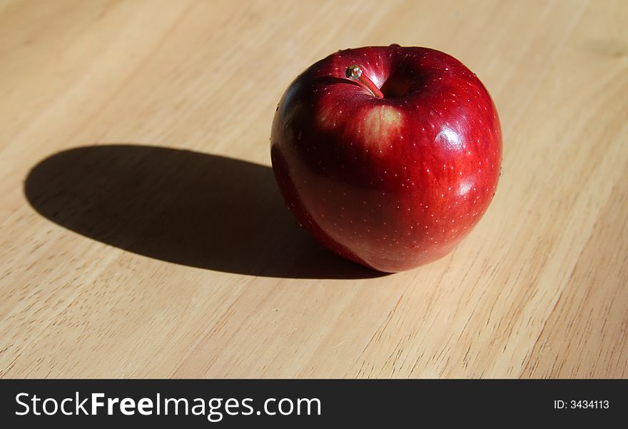 A single apple with hard lighting and a shadow