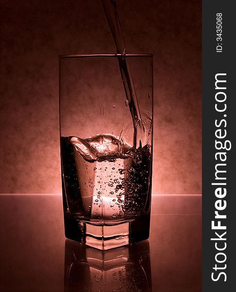 Water pouring into glass on red background. Water pouring into glass on red background.