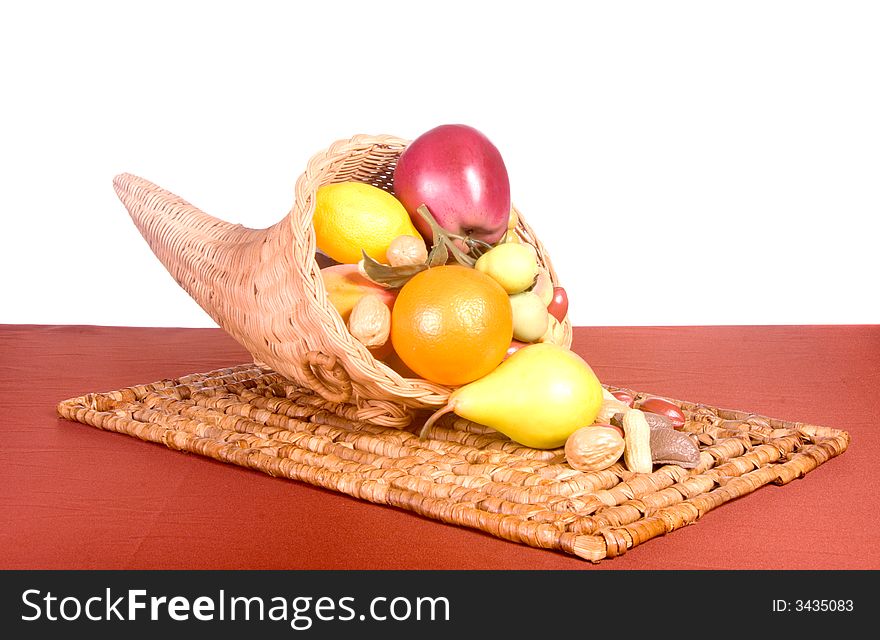 Wicker cornucopia filled with fruits and nuts on wicker placemat shot in studio over white