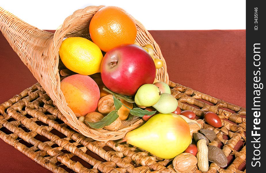 Wicker cornucopia filled with fruits and nuts on wicker placemat shot in studio over white