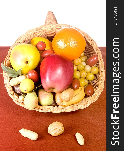 Wicker cornucopia filled with fruits and nuts on wicker placemat shot in studio over white