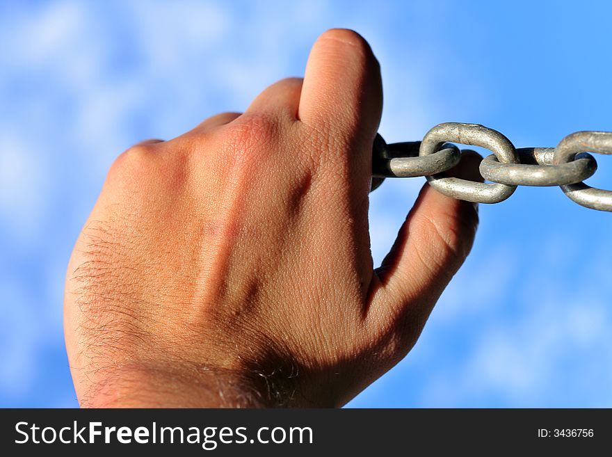 Hand holding chain against blue sky