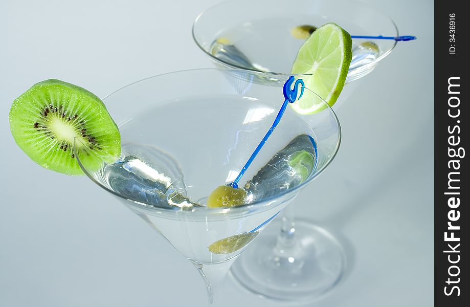 Martini glass with cocktail, green olive, lime and kiwifruit over white background closeup
. Martini glass with cocktail, green olive, lime and kiwifruit over white background closeup