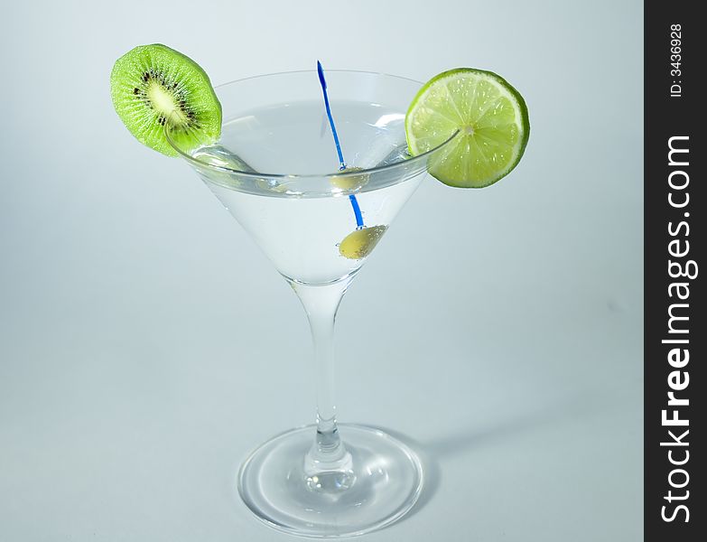 Martini glass with cocktail, green olive, lime and kiwifruit over white background. Martini glass with cocktail, green olive, lime and kiwifruit over white background