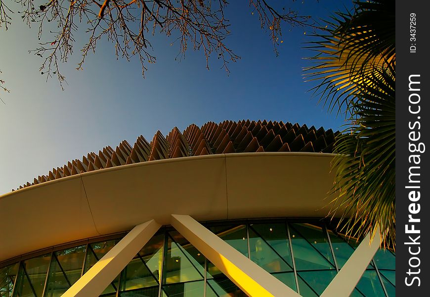 Branch tips of a barren tree, the huge fronds of palm trees and the spiky roof of the Singapore Esplanade Theater framing the graduated evening sky seen southwards. Branch tips of a barren tree, the huge fronds of palm trees and the spiky roof of the Singapore Esplanade Theater framing the graduated evening sky seen southwards.