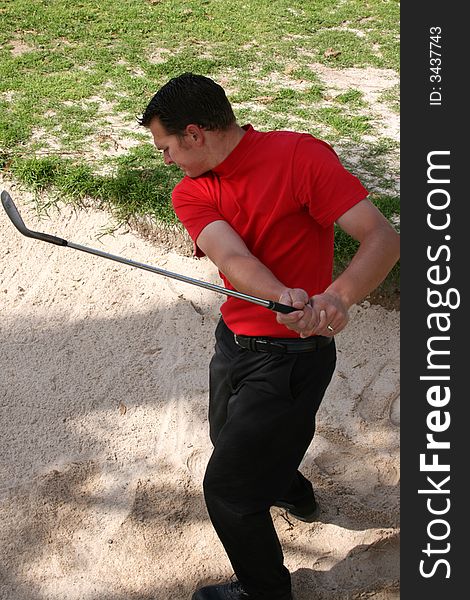 Young golfer hitting a shot out of the bunker taken from a side angle. Young golfer hitting a shot out of the bunker taken from a side angle