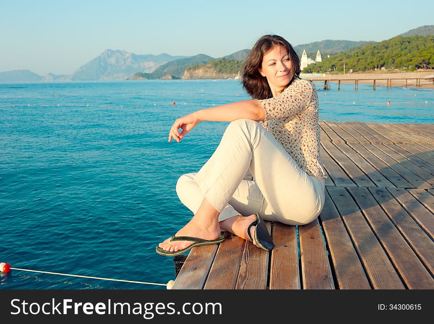 Girl sitting on a pier near the sea and looking to the side