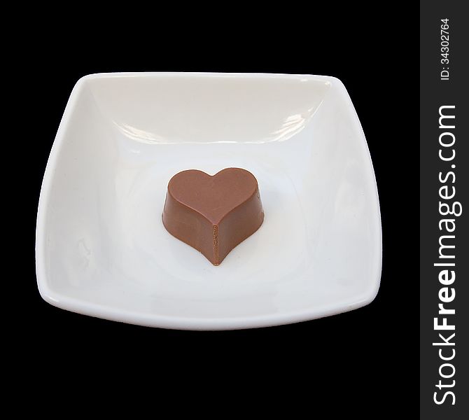 Studio isolated chocolate heart in a white plate over black background