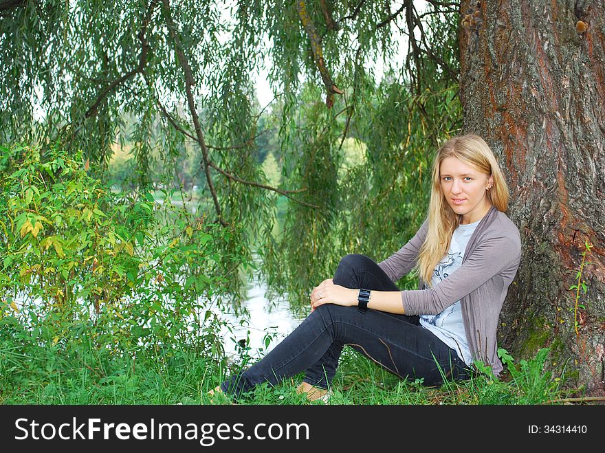 The girl sitting near willow near the lake.