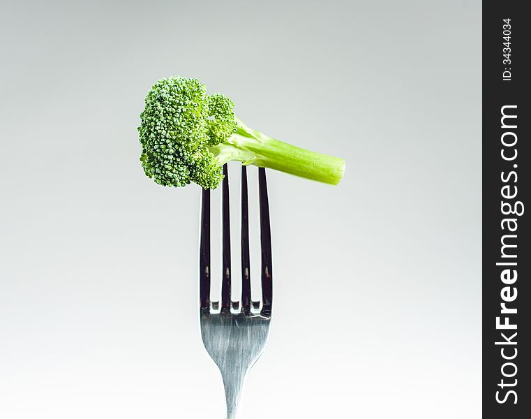 Broccoli on a fork over a gray white background