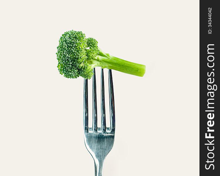 Broccoli on a fork over a warm gray white background