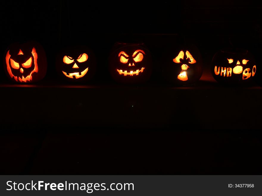 5 Halloween Jack O Lantern pumpkins illuminated in the dark night