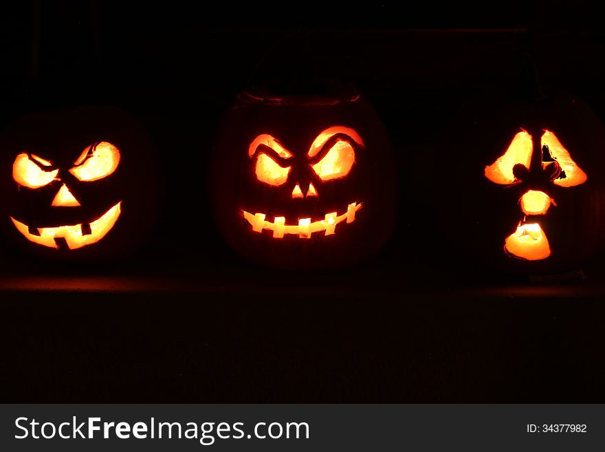 3 Halloween Jack O Lantern pumpkins illuminated in the dark night
