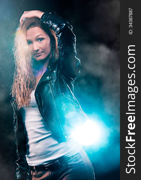 Portrait of amazing young woman with curly blond hair dressed in stylish black jacket. Over blue color spotlight. Portrait of amazing young woman with curly blond hair dressed in stylish black jacket. Over blue color spotlight.