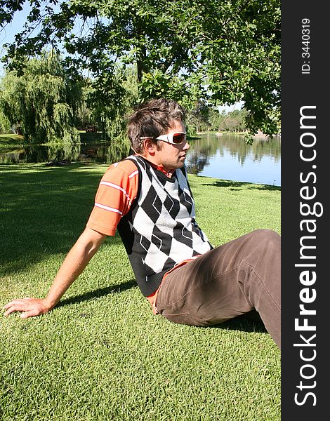 Young male model sitting in the park with water in the background. Young male model sitting in the park with water in the background