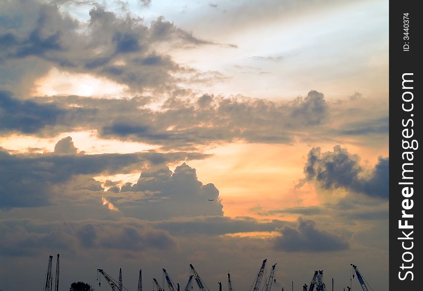 Cranes and an passenger aircraft silhouetted against stormy clouds as the sun breaks over the horizon. Cranes and an passenger aircraft silhouetted against stormy clouds as the sun breaks over the horizon.