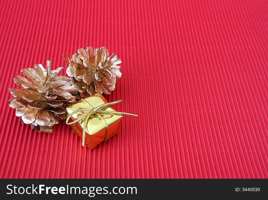 Small golden christmas gift and pine cones on a red background
