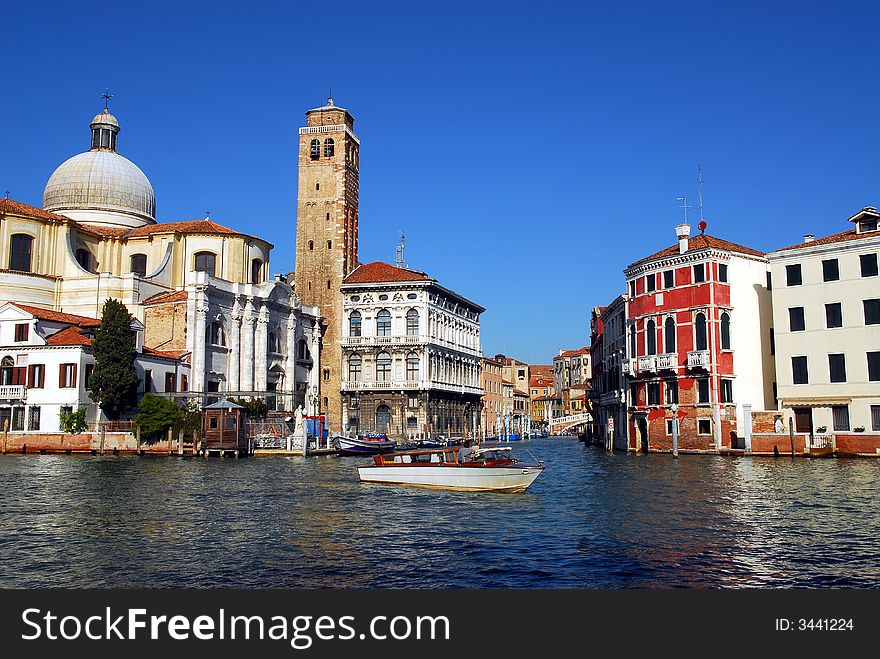 A taxi goes by on the Grand Canal with Chiesa di san Lucia church towering high in the compact architecture. A taxi goes by on the Grand Canal with Chiesa di san Lucia church towering high in the compact architecture.