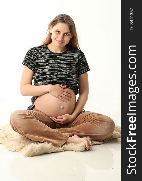 Happy young pregnant woman sitting on a floor and smiling. She is in black T-short , brown velvet pants. Happy young pregnant woman sitting on a floor and smiling. She is in black T-short , brown velvet pants