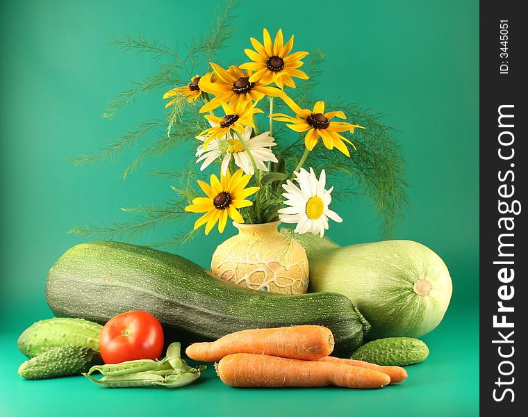 Still-life with vegetables and flowers on a green background.
