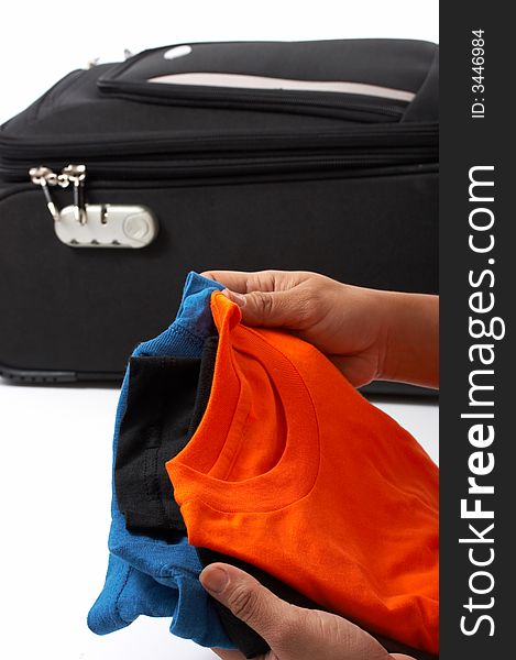 Hands holding shirts with a travel bag in the background. Hands holding shirts with a travel bag in the background