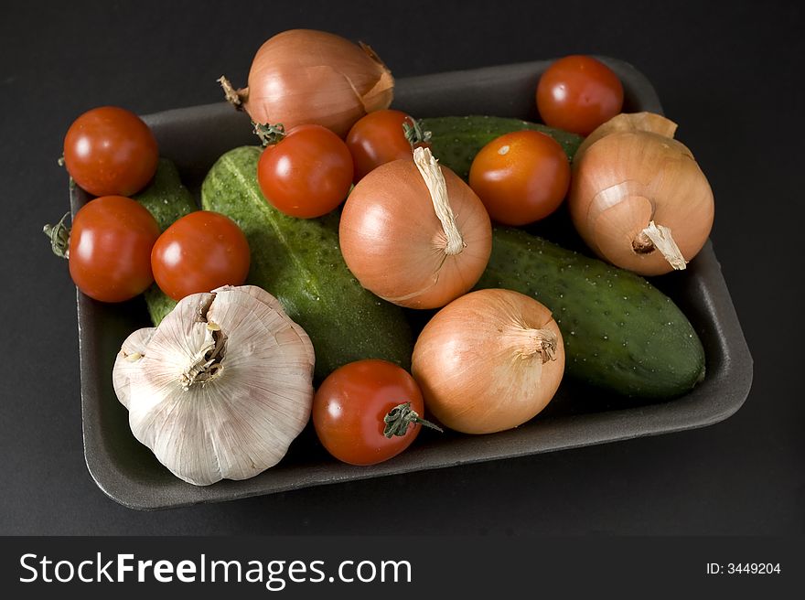 Onion and cucumber and garlic and tomato in plastic container over black background