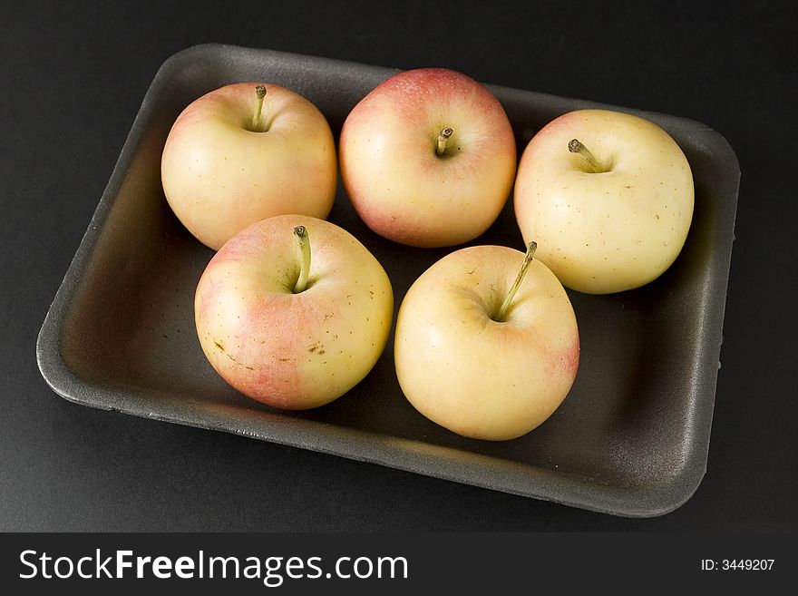 Apples in plastic tray over black background