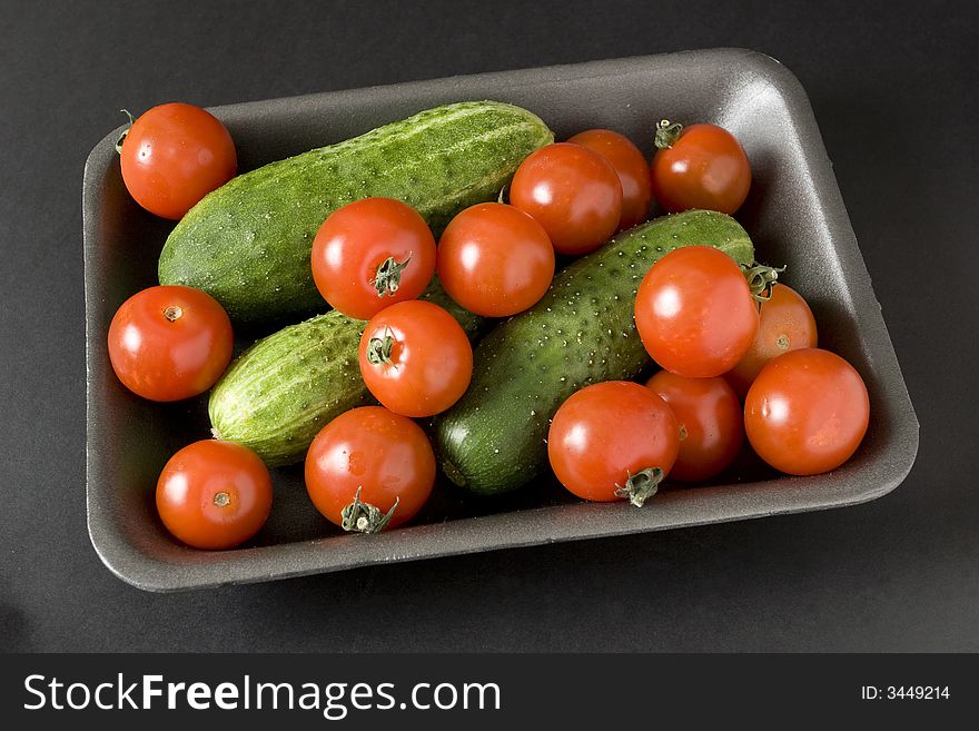 Tomatoes and cucumber in plastic container over black background
