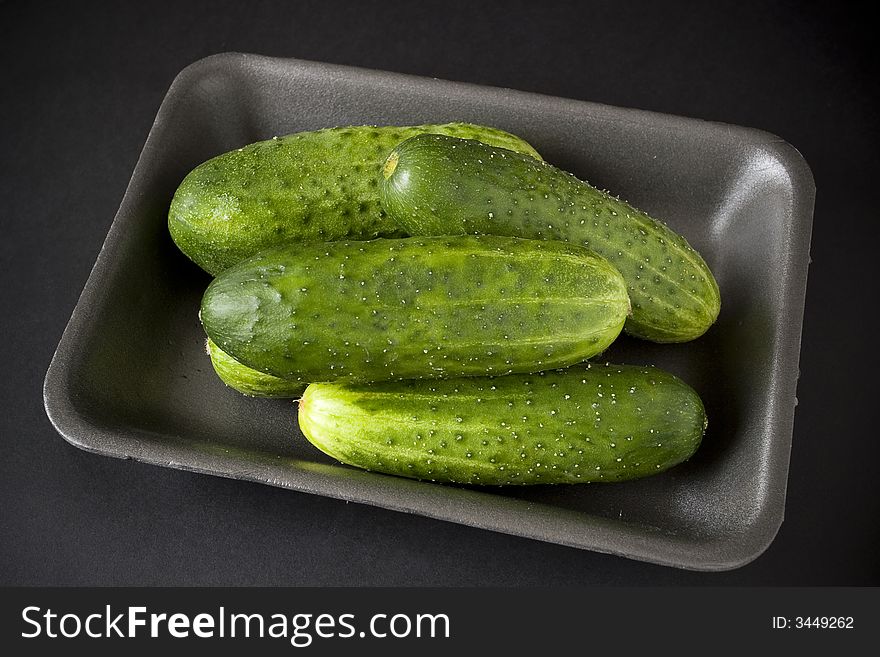 Cucumbers in plastic tray over black background