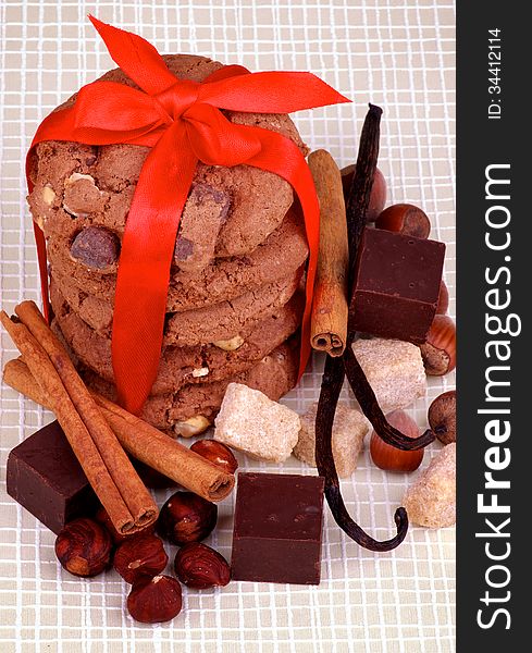 Stack of Delicious Christmas Cookies Tied with Red Ribbon and Chocolate Cubes, Nuts, Cinnamon Sticks and Vanilla Pods closeup on Checkered background