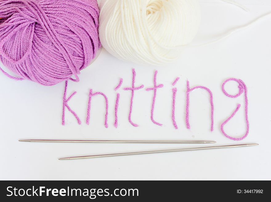 Written knitting with violet yarn, white and violet woolen skeins and knitted pieces.