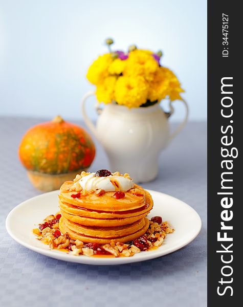 A stack of pumpkin pancakes with walnuts, cranberries, honey and yogurt