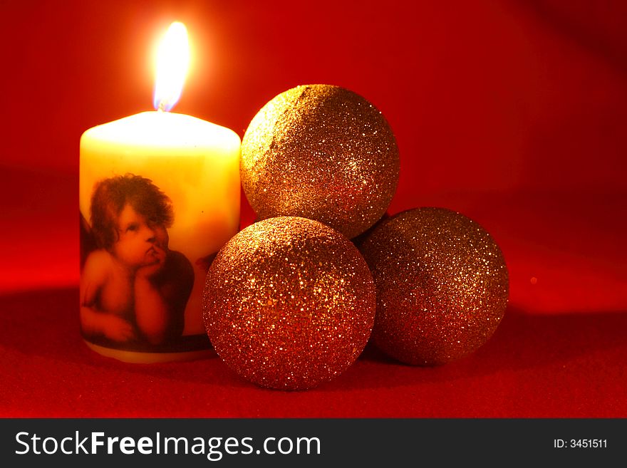 Candle with an angel and three christmas balls on a red background