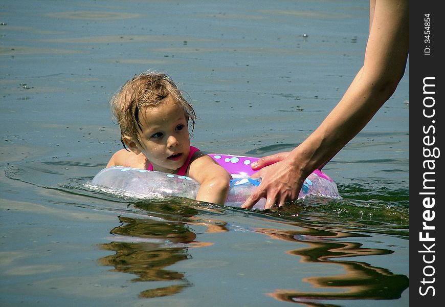 The girl bathes in the river on an inflatable circle supported by the mum. The girl bathes in the river on an inflatable circle supported by the mum