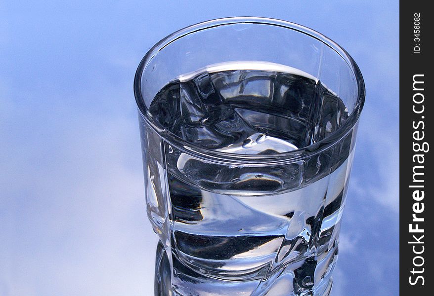 Glass of water on background with blue sky and clouds. Glass of water on background with blue sky and clouds