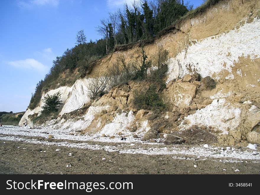 The falling cliff face with trees on the top, set against a blue sky. The falling cliff face with trees on the top, set against a blue sky