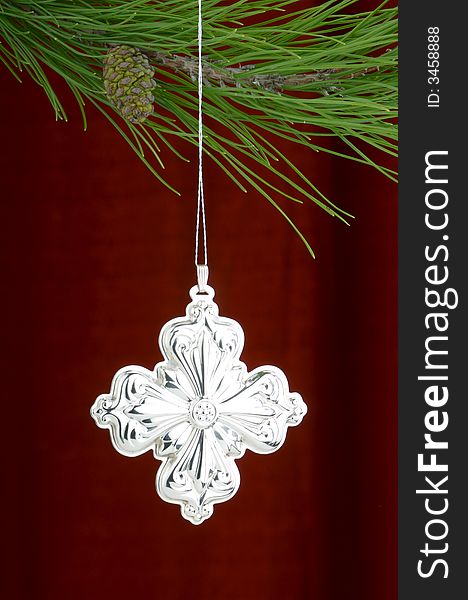 Christmas tree ornament with a pine tree branch in the top of the image, a silver cross decoration being the main focus. Christmas tree ornament with a pine tree branch in the top of the image, a silver cross decoration being the main focus