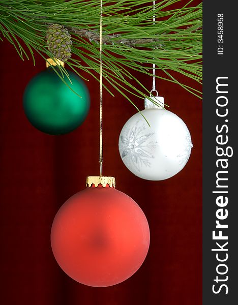 Three Christmas tree ornaments with a pine tree branch in the top of the image, a red decoration being the main focus. Three Christmas tree ornaments with a pine tree branch in the top of the image, a red decoration being the main focus
