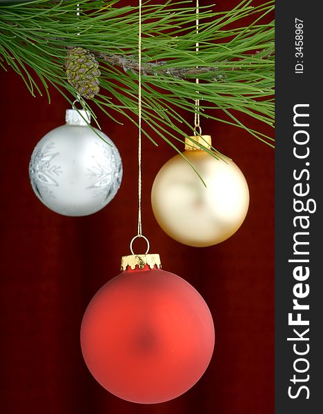 Three Christmas tree ornaments with a pine tree branch in the top of the image, a red decoration being the main focus. Three Christmas tree ornaments with a pine tree branch in the top of the image, a red decoration being the main focus