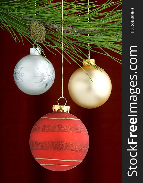 Three Christmas tree ornaments with a pine tree branch in the top of the image, a red, gold decoration being the main focus. Three Christmas tree ornaments with a pine tree branch in the top of the image, a red, gold decoration being the main focus