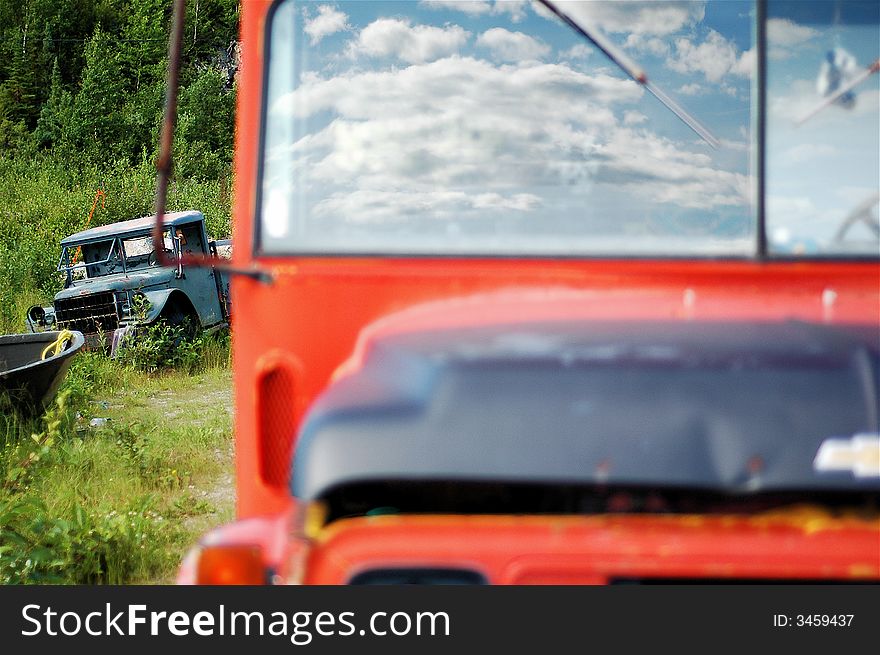 An abandoned bus sits out of focus in the foreground with fluffy clouds reflected perfectly in the windshield. in the background a broken down landrover sits in sharp focus. An abandoned bus sits out of focus in the foreground with fluffy clouds reflected perfectly in the windshield. in the background a broken down landrover sits in sharp focus.