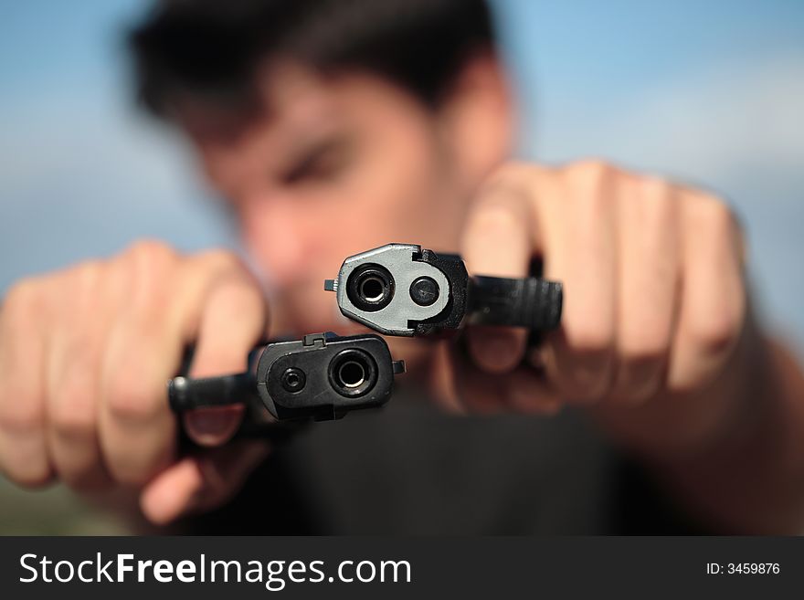 A young, robust man, in his 20's with dark hair pointing 2 pistols to the camera. A young, robust man, in his 20's with dark hair pointing 2 pistols to the camera.