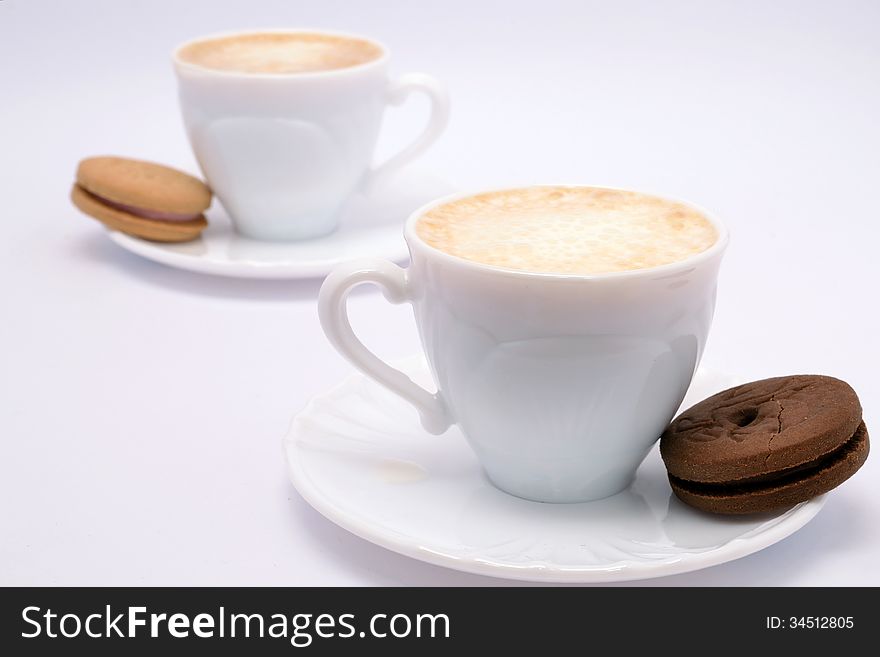 Coffee with milk and cream in beautiful fine china cups accompanied by vanilla and chocolate cookies. Coffee with milk and cream in beautiful fine china cups accompanied by vanilla and chocolate cookies