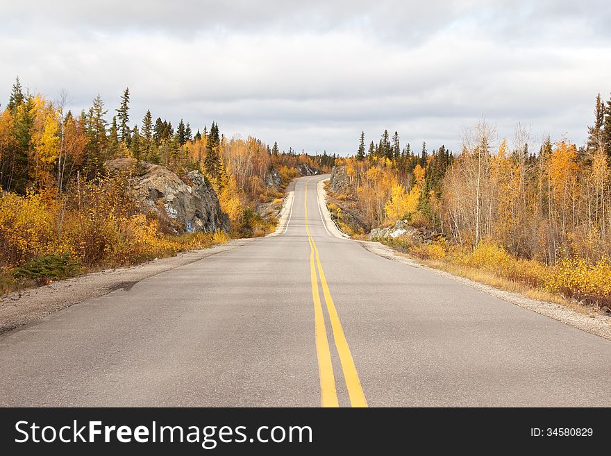 A curved highway through a forest of fall colored trees and a cloudy sky overhead. A curved highway through a forest of fall colored trees and a cloudy sky overhead