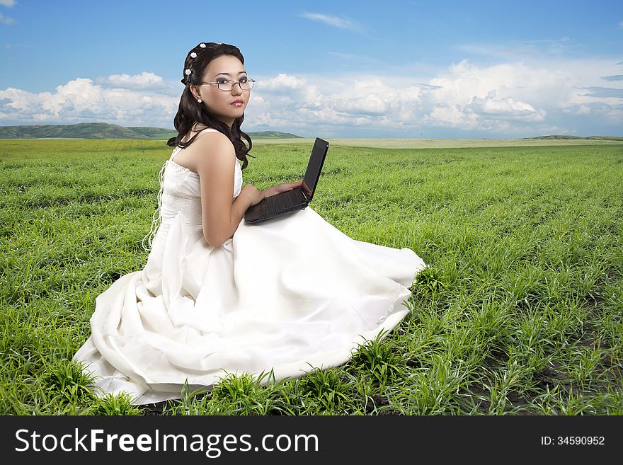 Girl in a long white dress, sitting on a grass with the computer