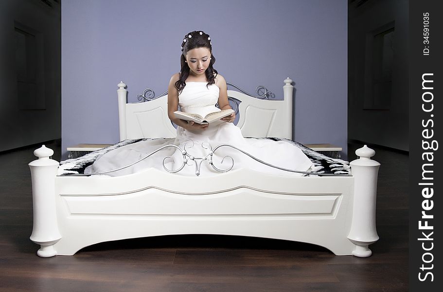 Girl in a long dress on a white bed reads the book. Girl in a long dress on a white bed reads the book