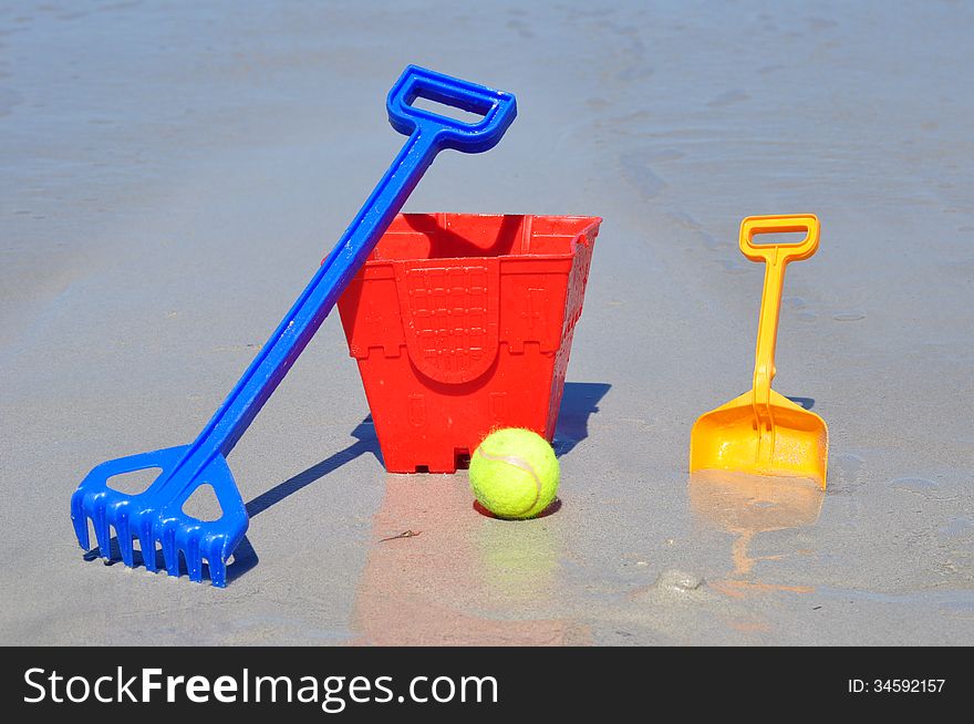 Red bucket spade ball and rake on the beach in a group