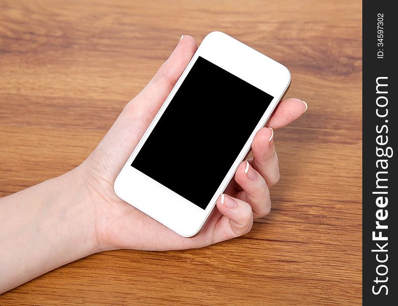 Woman hand holding a touch white phone with black screen against the background of a wooden table. Woman hand holding a touch white phone with black screen against the background of a wooden table