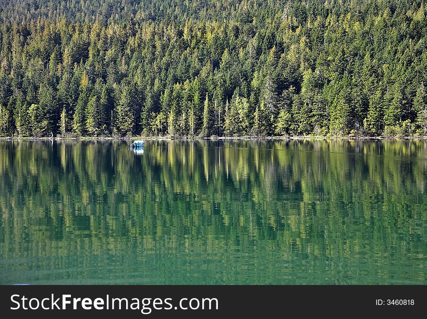 A white boat on the lake surrounded by a dense wood. A white boat on the lake surrounded by a dense wood